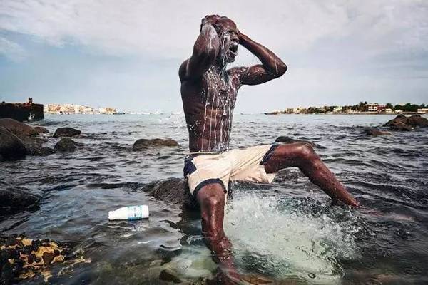 　　在非洲大陆西部凸出部位最西端的国家，有一项运动风靡至极，它充斥着强烈的男性荷尔蒙味道，夹杂着特殊的族群信仰以及无数人对于名利声望的渴望。这个国家叫塞内加尔，这项运动叫摔跤。  　　    　　(Lac de Guiers在运动场围栏外，观看即将开始的一场大型的摔跤比赛。)  　　Lac de Guiers曾经塞尔维亚摔跤场上以硬拳闻名的明星选手，退役之后经营着一家摔跤训练学校，和家人过上了令人羡慕的生活。  　　现在的他依然会经常出现在熟悉的运动场，只是换了一个身份，以教练或者观众的视角，看着场上改变他人生的比赛。  　　    　　(超级明星，摔跤手巴拉·盖伊二世(Balla Gaye2))  　　在塞内加尔国内最受关注的明星选手，他们能出入健身房接受高级而专业的训练，赢得一场大型比赛最多可获得20万美元奖金。退役以后，有像Lac de Guiers一样选择开设摔跤训练学校、担任教练、大厦保安等诸多职业选择……  　　而这一切对于以农业生产为主，失业率高达50%，人均年收入仅为980美元(约合人民币6000元左右)国度里的普通民众来说，是不可想象的。  　　    　　(德吉布里尔结束了一个学期的学习，乘坐便车回吉贝林村。)  　　德吉布里尔是济金绍尔(塞内加尔南部最大的城市)吉贝林村备受瞩目的年轻摔跤手。在外求学的他，每到放假便会回到家乡帮助家人做农活。  　　结束从早到晚的农活，德吉布里尔会叫上同村其他的摔跤手去海滩边，一起进行跑步和摔跤训练，为村里的摔跤节做准备。在摔跤比赛到来之前，德吉布里尔的妹妹还特地为他写了一首歌，希望能给哥哥带去勇气和好运。  　　在这里摔跤已经超出了一般运动项目的范畴，它更多被赋予了个人价值、社会地位与期盼、宗教意义等庞大的社会附加价值。成为一名职业摔跤选手，被当做一条摆脱贫困的捷径，它就像一只幻象中的藏宝箱，呼唤着一个又一个有体格有梦想的年轻人投身其中。  　　    　　在塞内加尔国内，这项被人民视为“国粹”一样的体育运动，在最初时，仅仅是村落里的男人们在丰收之后聚集在一起，怀着喜悦的情绪，进行的庆祝活动。随着时间流逝，慢慢被赋予了更多的内容和价值使命，成为了现今塞内加尔最受欢迎的流行运动。  　　    　　(巴拉·盖伊二世和伊缪·先尼赛前宣传海报出现在街头)  　　在城市里，大型摔跤比赛的的盛况堪比当地的总统选举，关于赛事的巨幅海报，在比赛出来的前几周便被挂上了人头攒动的街头，在这座城市里，进行着一场运动的“高逼格”预热。  　　    　　    　　(赛场/街边的两处公共电视机前，围满了观看比赛的市民。)  　　比赛到来，被炎热空气笼罩着的城市，沉浸在全民狂欢的情绪中。两万人的体育场馆内座无虚席，而对于因为种种原因无法前往赛场的人来说，聚集在街道上公共电视机前观看摔跤比赛亦是一种参与其中的方式。  　　    　　(比赛前，妇女拉拉队进行助威表演)  　　在整个比赛过程中，击鼓、舞蹈还有妇女拉拉队的表演、摔跤轮番上演，他们就像是在举办一场传统庆典仪式一般进行着一场摔跤比赛。  　　    　　上场前摔跤手们在腰间缠绕上一块特殊的彩布，激烈而残酷的比赛开始，两个摔跤手在沙地上相互角力，双方都竭尽全力试图将另一方摔倒在地。在塞内加尔摔跤规则中，一方四肢同时着地，或者背部着地又或者被摔出摔跤场，则被判为输家。  　　与我们印象中的摔跤不同，塞内加尔摔跤因蕴含其中的巫术和魔法使它被赋予了独特的神秘色彩。这一系列神秘的仪式，塞内加尔人称之为Gris-gris，是摔跤比赛必不可少的一部分。  　　    　　在塞内加尔的传统观念中，水是魂魄栖息之地。所以在赛前几天，有的摔跤选手会在水中用牛奶洗澡，他们相信这种方法能使自己与水中的灵魂相连，从而获得特殊的能量。  　　    　　(赛前，一位萨满在祭祀摔跤手先人的地方供奉牛奶。以期赶走厄运，带来好运。)  　　    　　(比赛开始前，摔跤手正在将特殊药水淋在自己的身上)  　　到了比赛开始前，摔跤手们会从巫师手中买入特制的驱邪护身符和特殊药水, 里面包括狮子和鬣狗的毛发、瞪羚的奶水、神圣树木的根茎等。并且将药水涂抹在身上，他们相信这能带来超能力，从而提高自己获胜几率。  　　甚至每个摔跤手都会配有一位助理，为比赛做祭祀并帮他们照看护身符。这所有的一切都为这项与力量、技巧相关的运动，添设了不一样的外衣。  　　但是，其实在这件神秘外衣之外，有一个因素才是对摔跤手的命运起到真正决定性作用的——经纪人。塞内加尔的职业摔跤是在残酷的淘汰机制下进行的，一个摔跤手的职业生涯的长度，取决于他什么时候输。但是一个摔跤手的职业生涯什么时候开始，则取决于他什么时候能获得上场比赛的机会，而这一切都掌握在经纪人的手中。  　　它就像一场关于命运的赌博，即使决定胜负的牌掌握在别人的手上，人们也愿意奋力一搏， 赢的人获得一切，巨额的奖金，万人的簇拥。而输的人始终是一无所有。  　　    　　每个来到海滩上的年轻人都不留余地投入训练之中，他们在等待一位发现自己的伯乐;等待一个由社会底层向顶层翻身的机会。但是机会只有一个次，每个人都心知肚明。  　　文章来自：有马体育